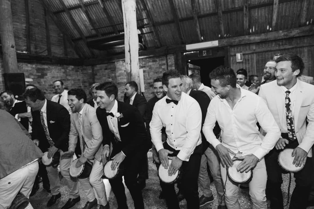 Black-and-white photograph of men playing hand drums in a row.