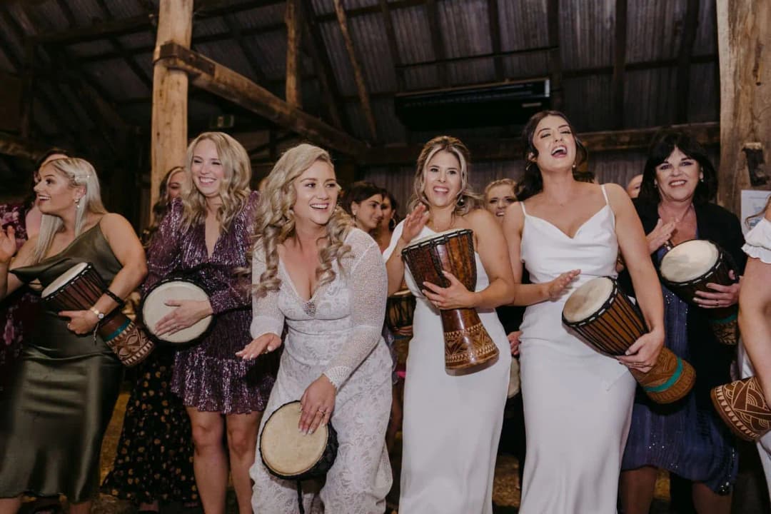 Bride and several women playing hand drums together inside the reception room.