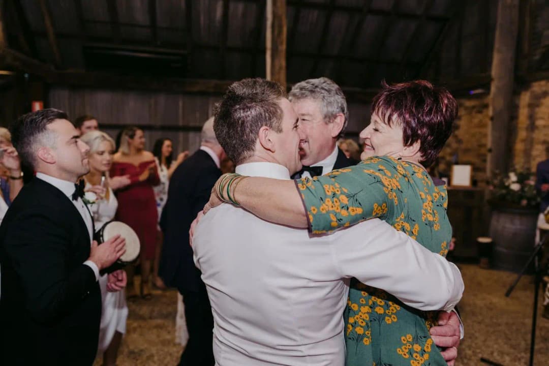 Groom embracing two guests while another man watches on the dance floor.