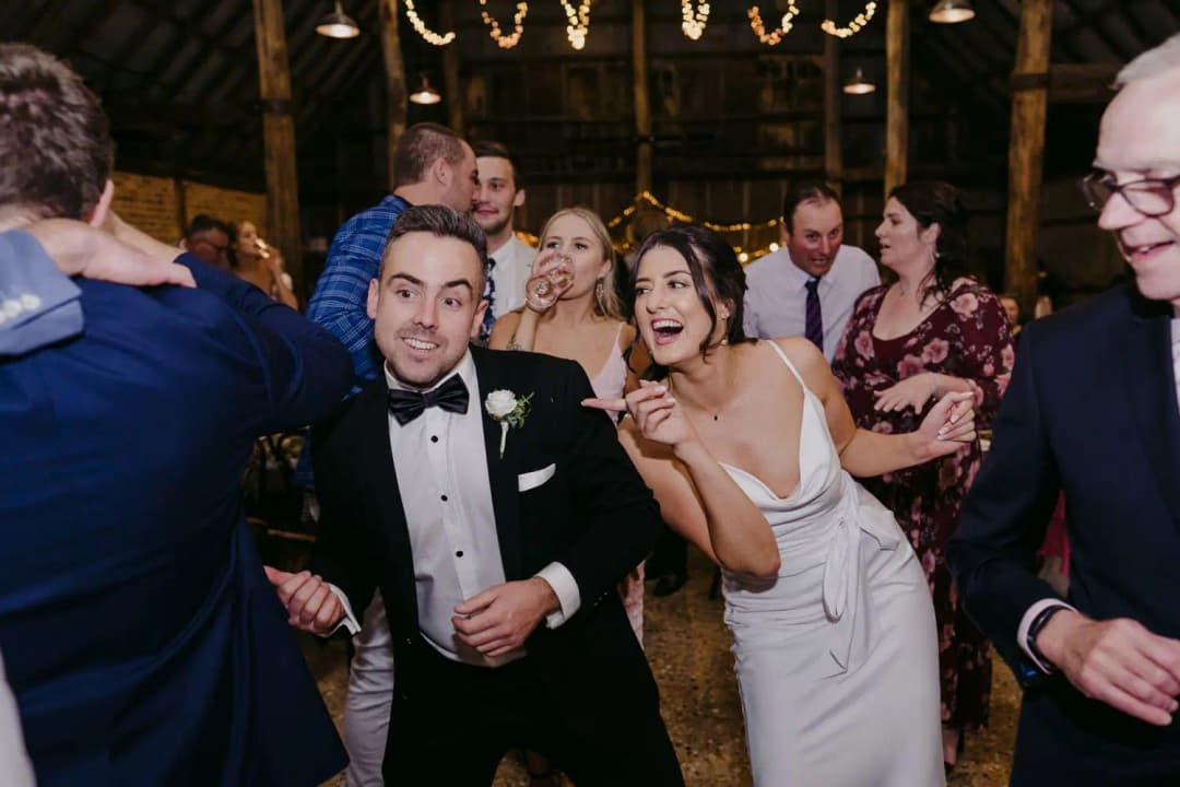 Guests smiling and dancing together beneath reception string lights.