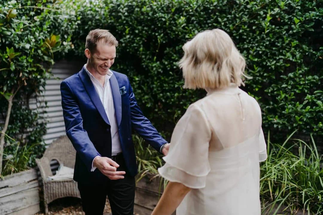 Groom holding his arms open toward the bride in a backyard