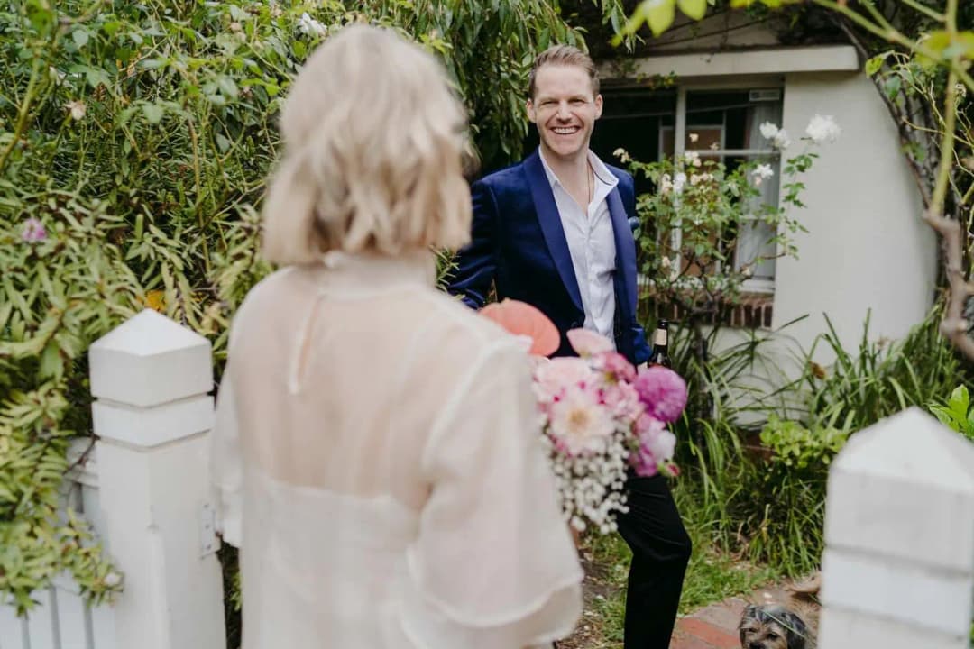 Groom smiling at the bride beside a leafy garden gate