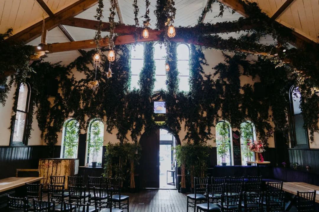 Ceremony chairs beneath hanging greenery and timber roof beams