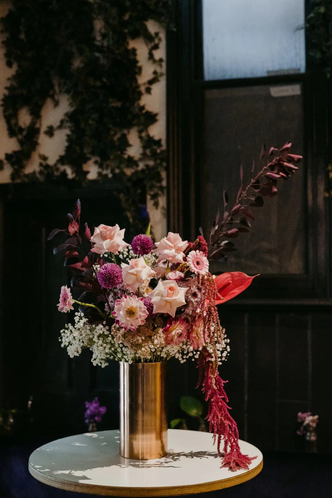 Pink and peach flower arrangement in a gold vase on a small table