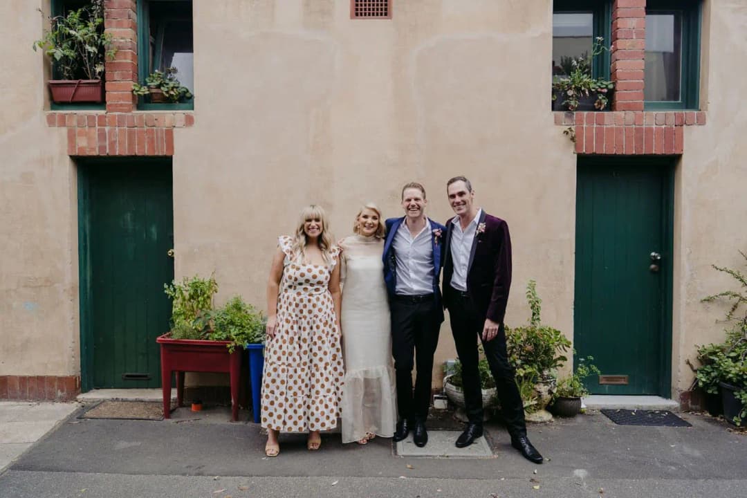 Four wedding party members posing together outside two green doors