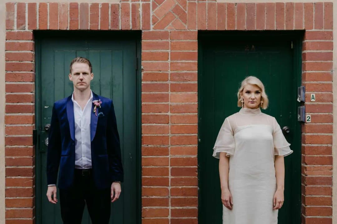 Bride and groom standing separately in green doorways framed by red brick