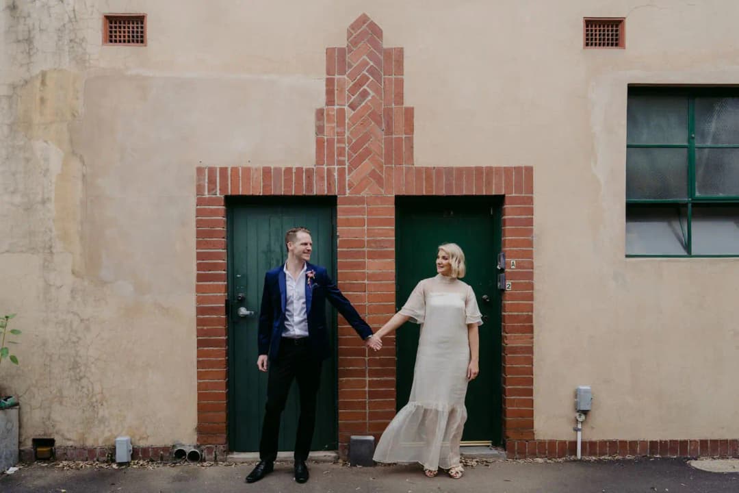 Bride and groom holding hands between two green doorways
