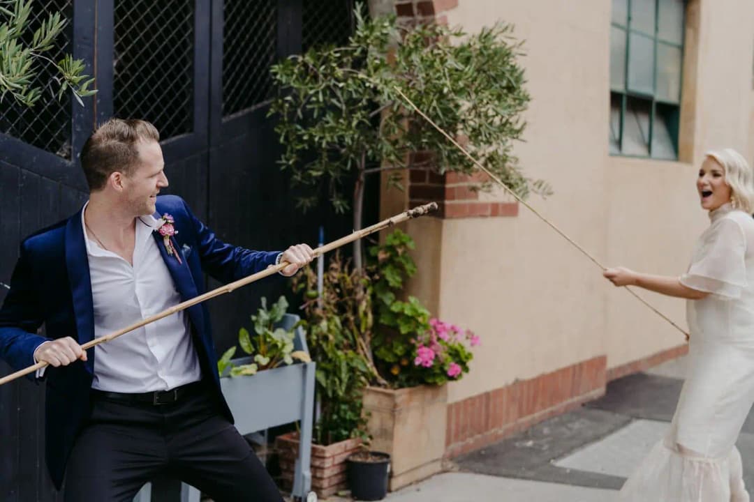 Groom grinning while holding a bamboo pole opposite the laughing bride