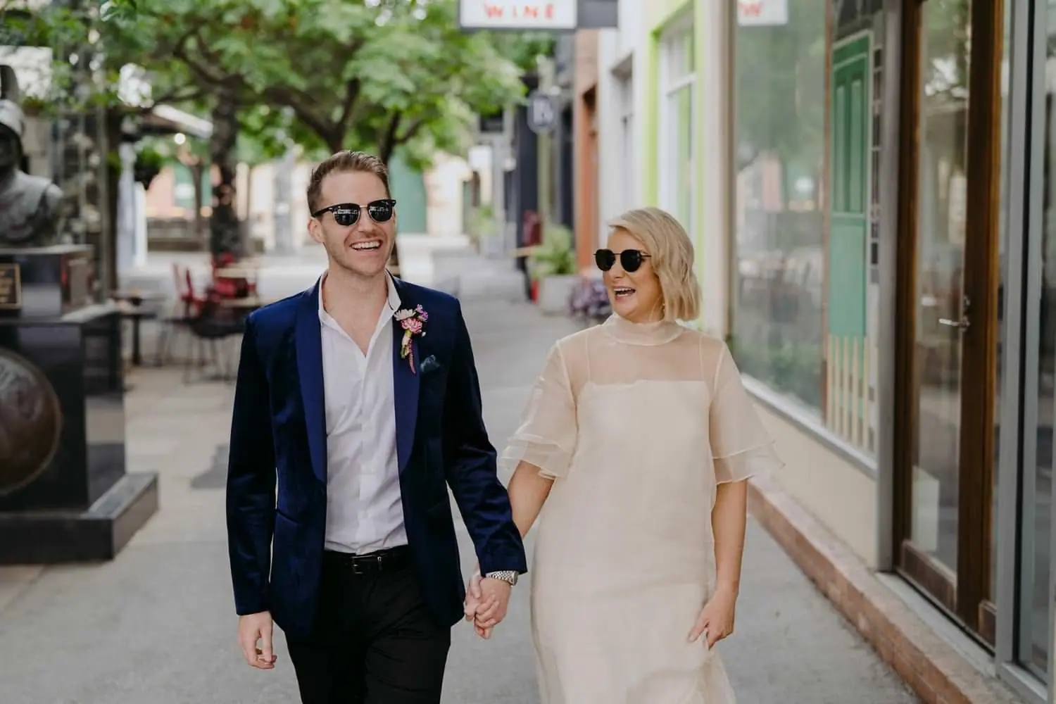 Bride and groom wearing sunglasses while holding hands on a shopping street