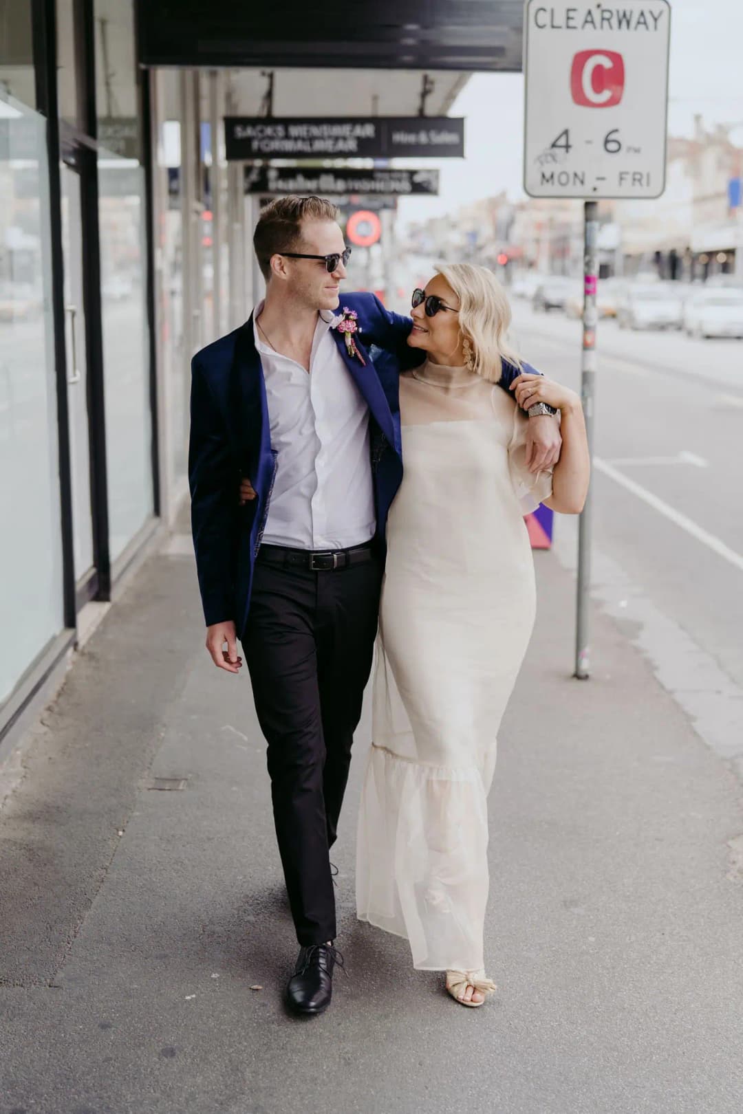 Bride and groom walking arm in arm beneath shop awnings