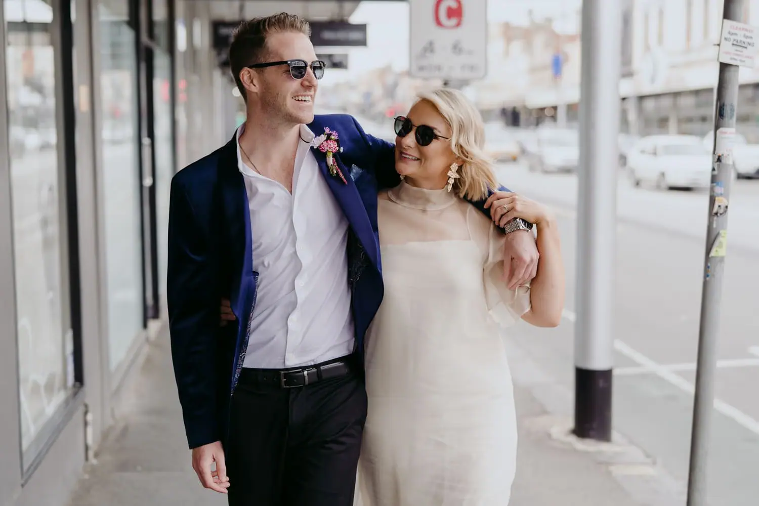 Bride and groom laughing in sunglasses with his arm around her shoulders