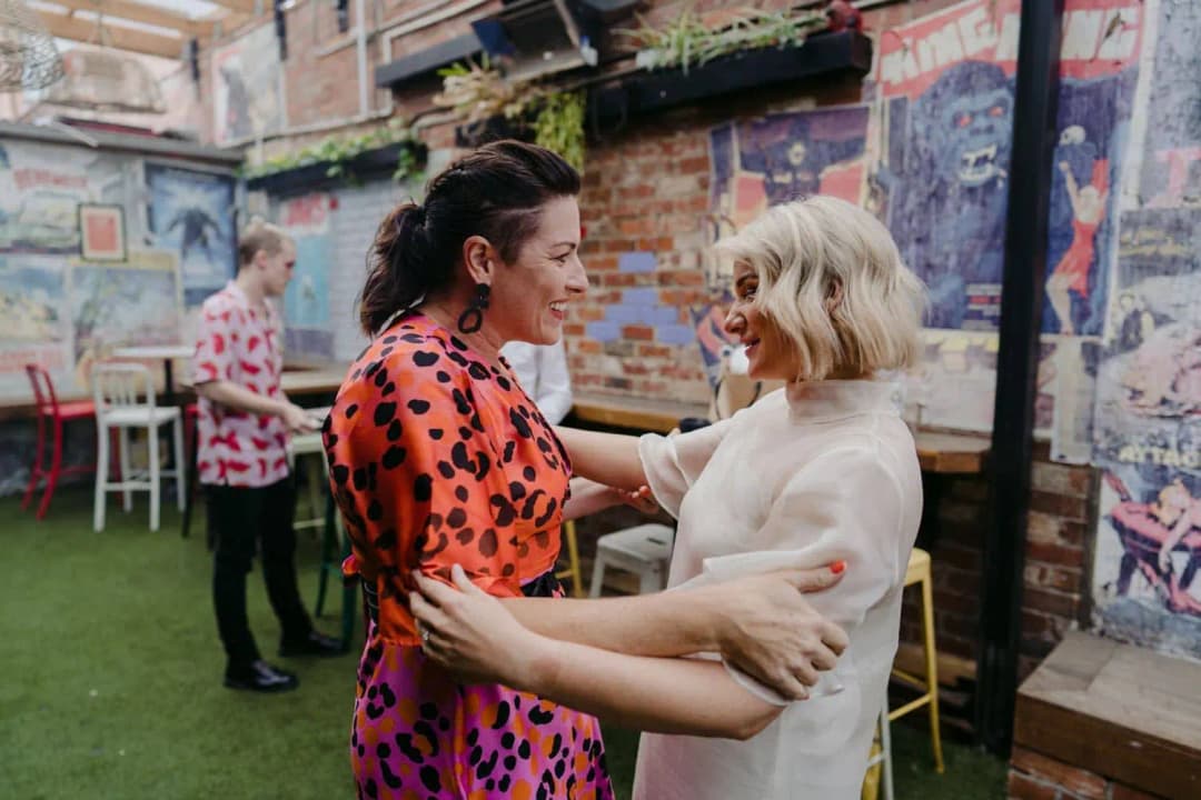Bride greeting a woman in an orange patterned dress in a courtyard