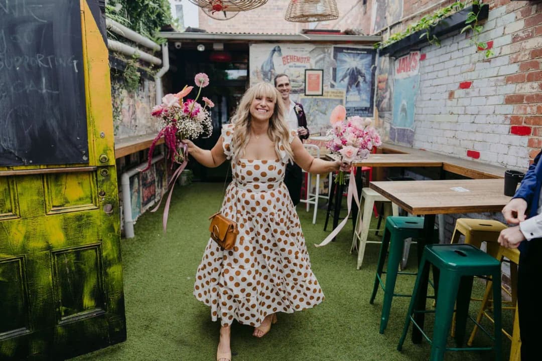 Smiling bridesmaid holding two pink bouquets in a colourful courtyard