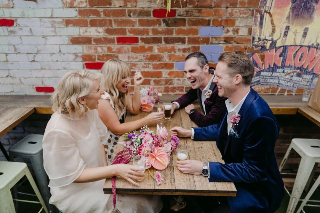Four wedding party members laughing over drinks at a courtyard table