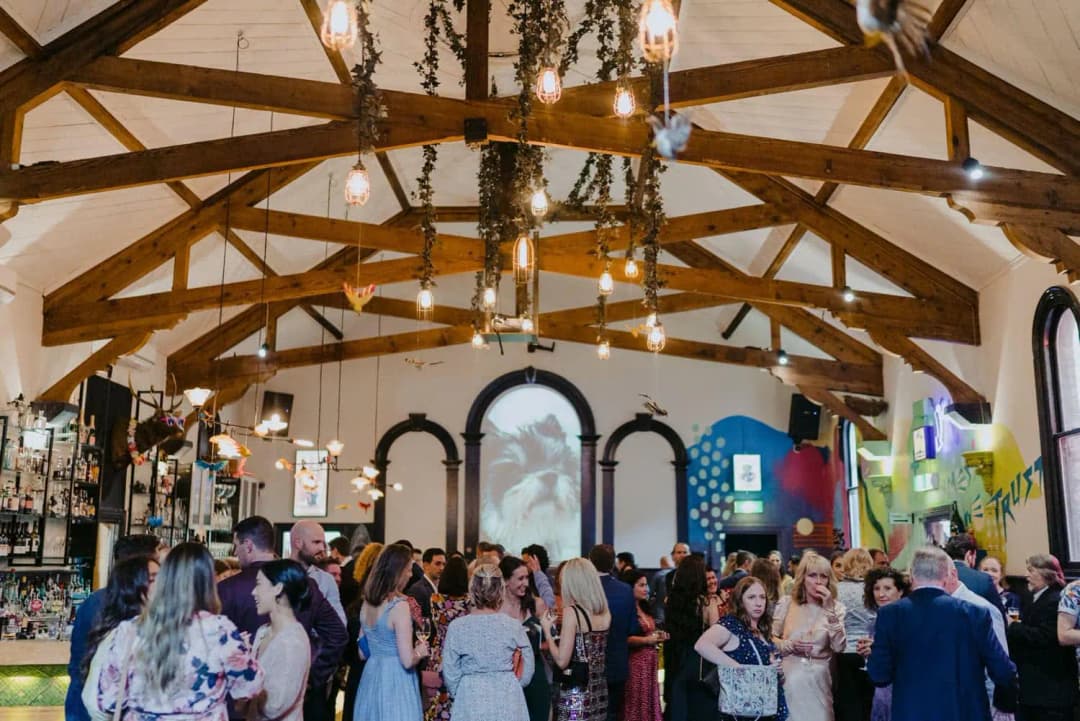 Wedding guests gathered beneath timber roof beams and hanging greenery