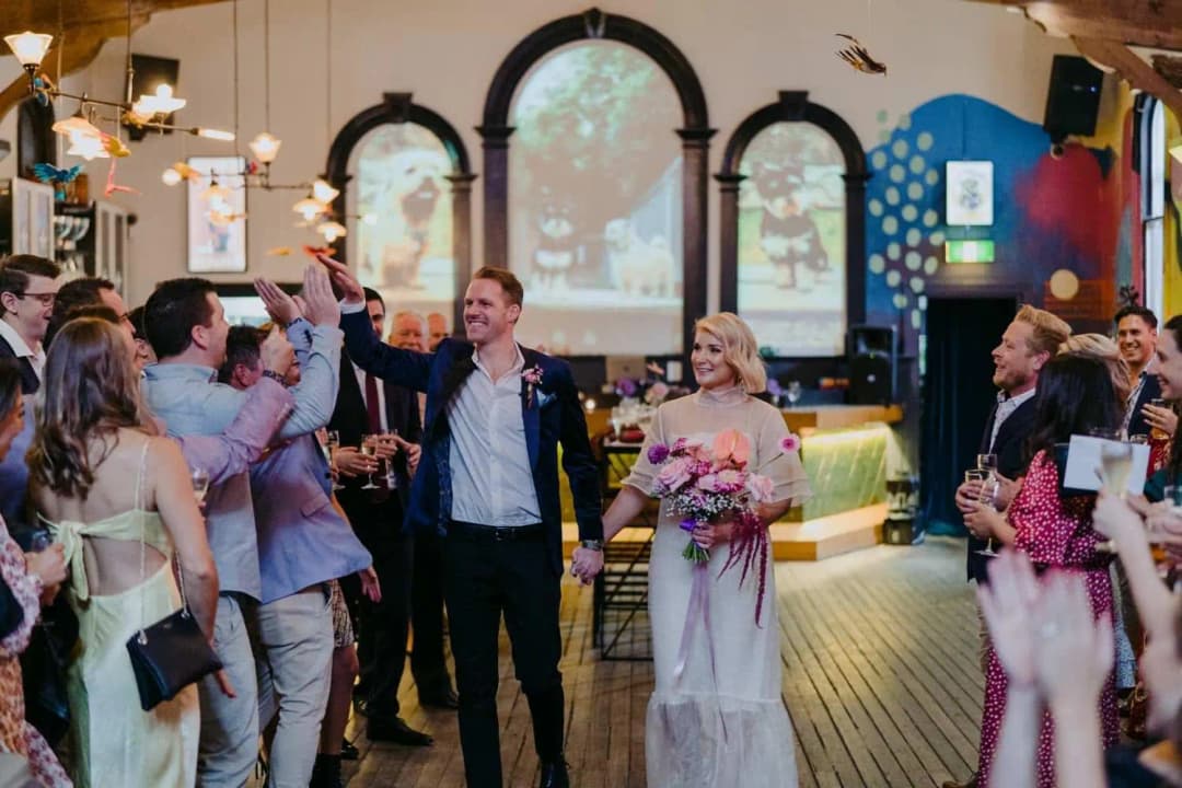 Bride and groom walking into the ceremony as guests raise their hands