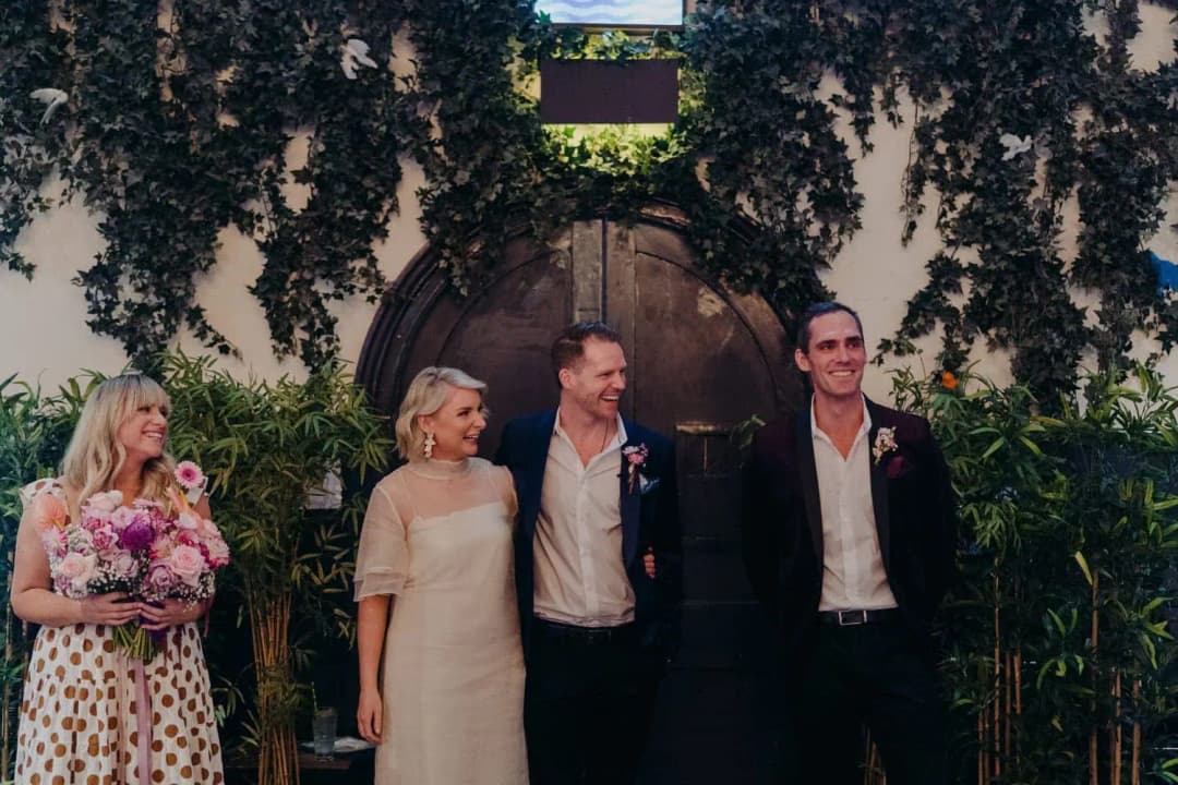 Wedding party standing beneath hanging greenery in front of an arched door