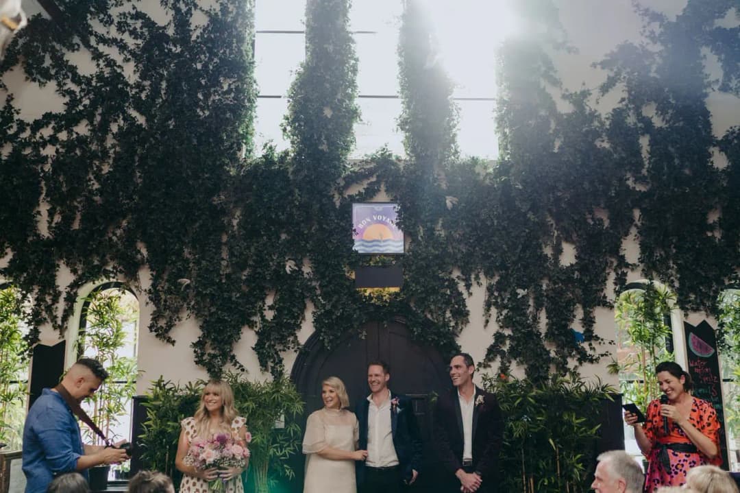 Wide view of the wedding ceremony beneath tall windows and hanging greenery