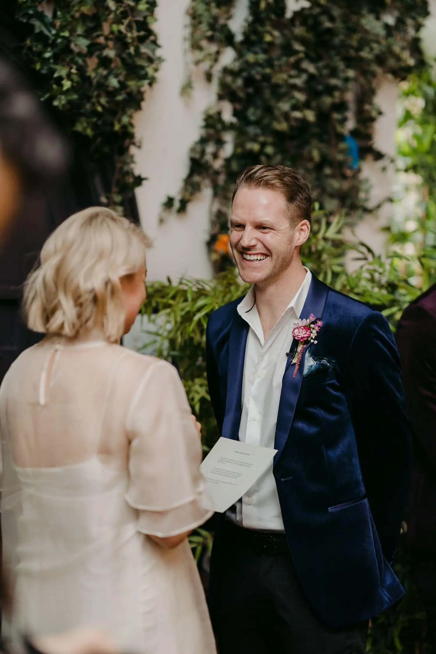 Groom smiling as the bride reads from a sheet of paper