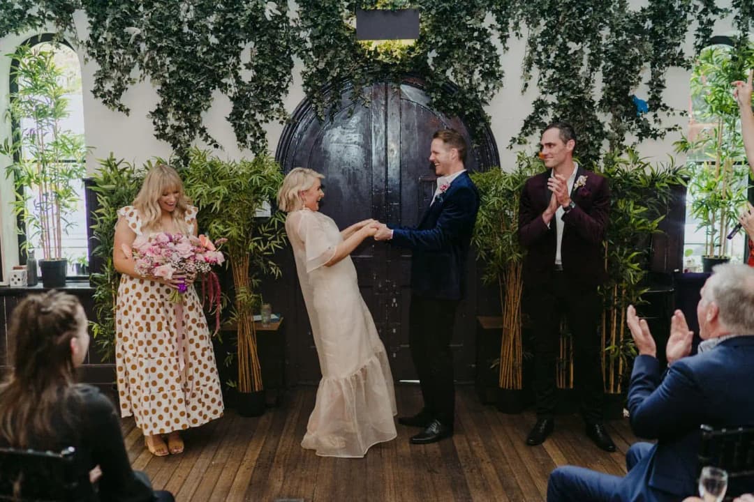Bride and groom holding hands as guests applaud during the ceremony