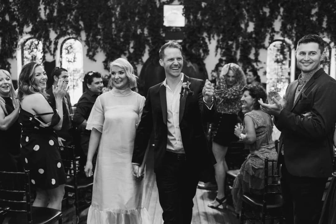 Black and white photograph of the bride and groom walking through applauding guests