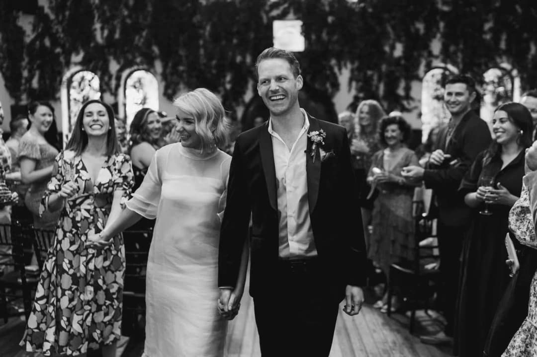 Black and white photograph of the couple smiling as guests celebrate around them