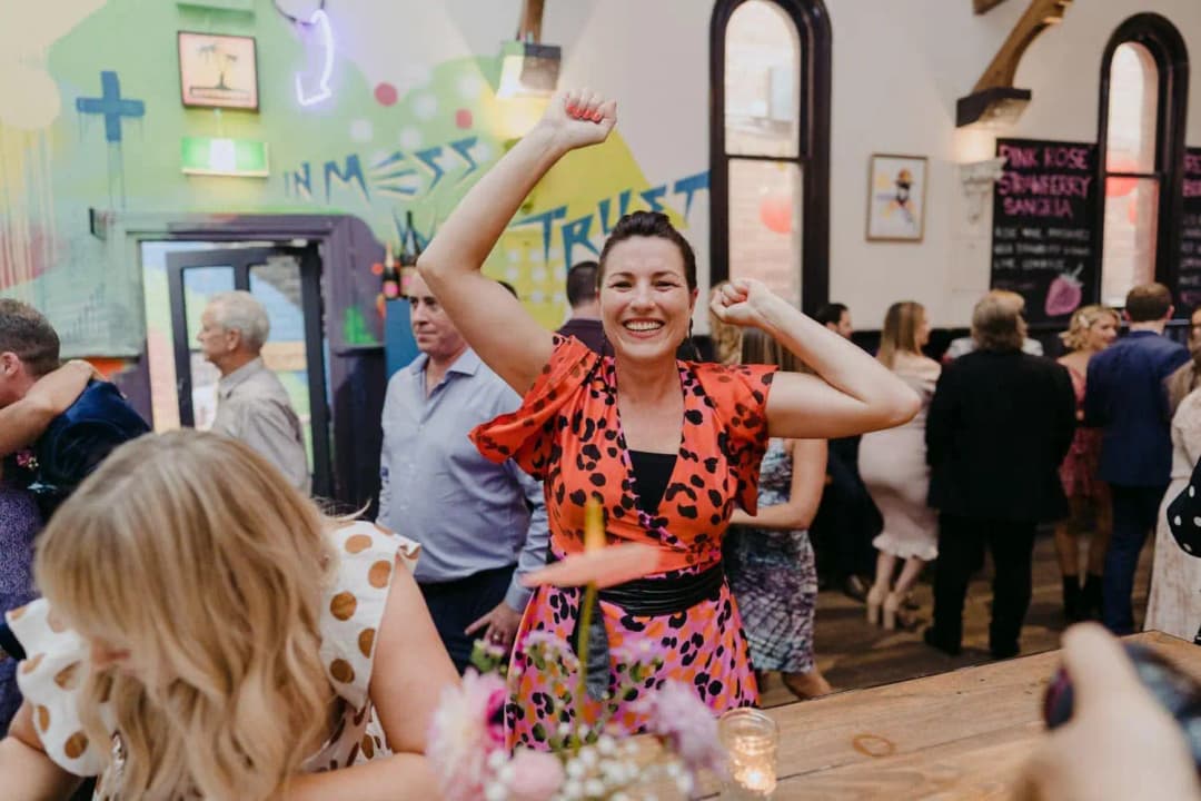 Woman in an orange patterned dress raising her arm and smiling at the reception