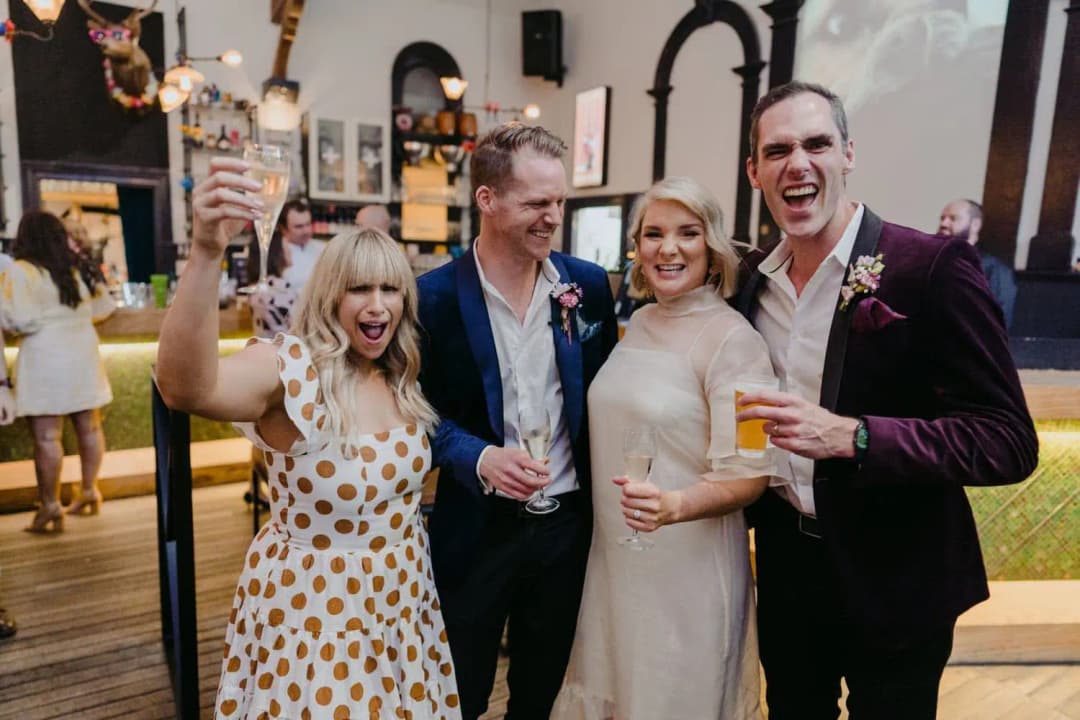 Bride and groom posing with two wedding party members holding drinks