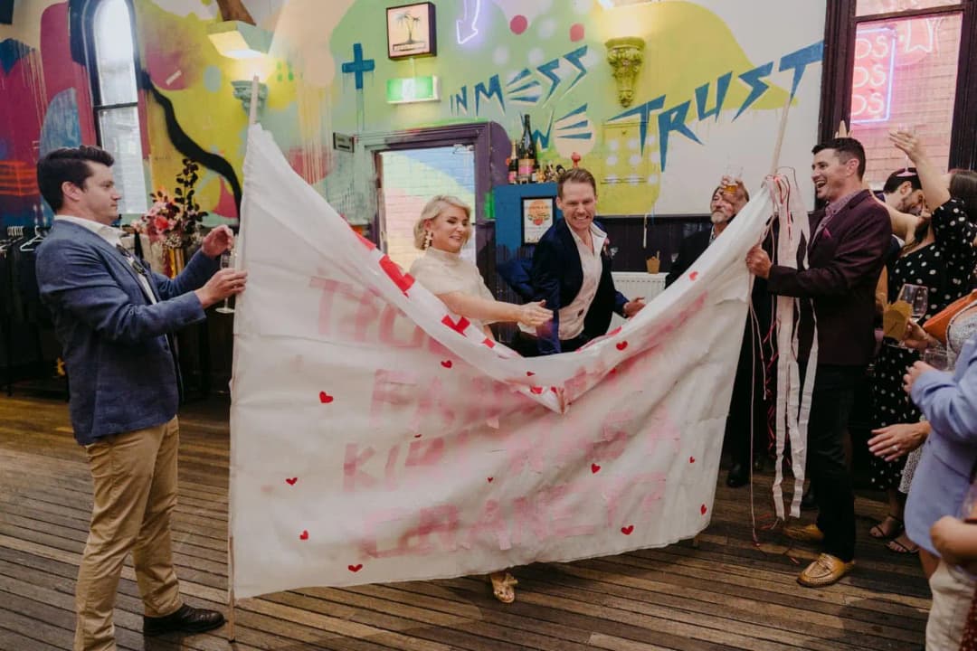 Bride and groom standing behind a paper banner decorated with red hearts