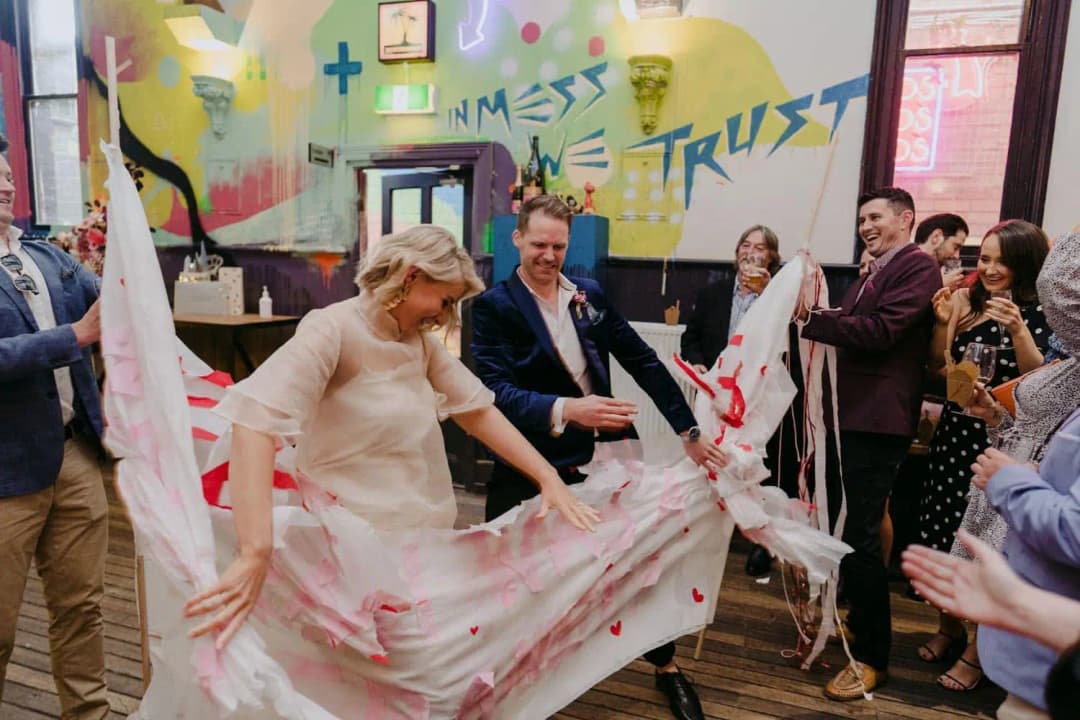 Bride stepping through a torn paper banner as guests cheer