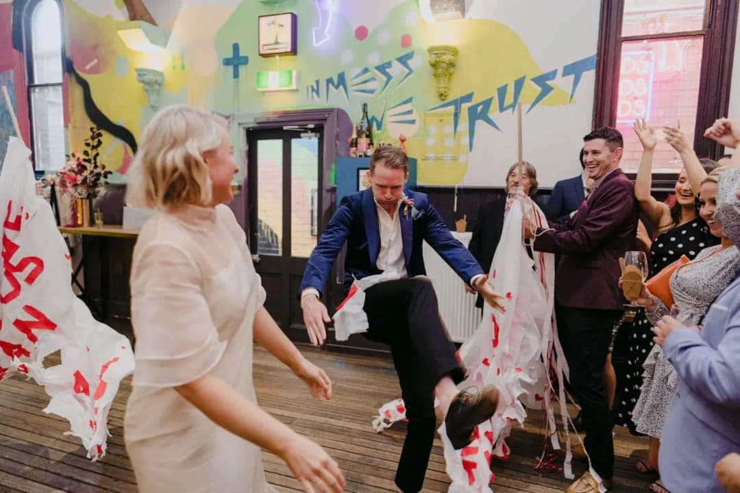 Groom stepping through a torn paper banner beside the smiling bride