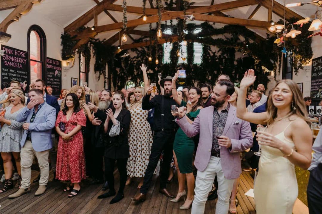 Wedding guests cheering and applauding beneath the venue's timber roof