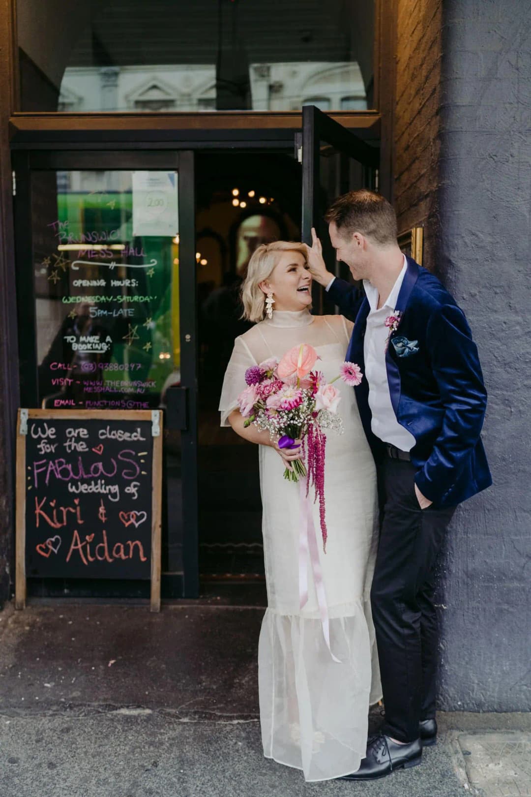 Bride and groom embracing outside a shop doorway with a pink bouquet