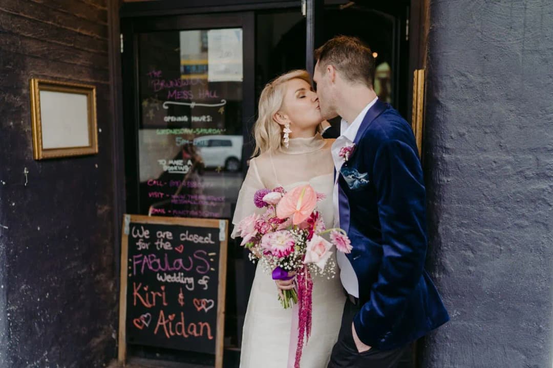 Bride and groom kissing outside a shop doorway beside handwritten signs