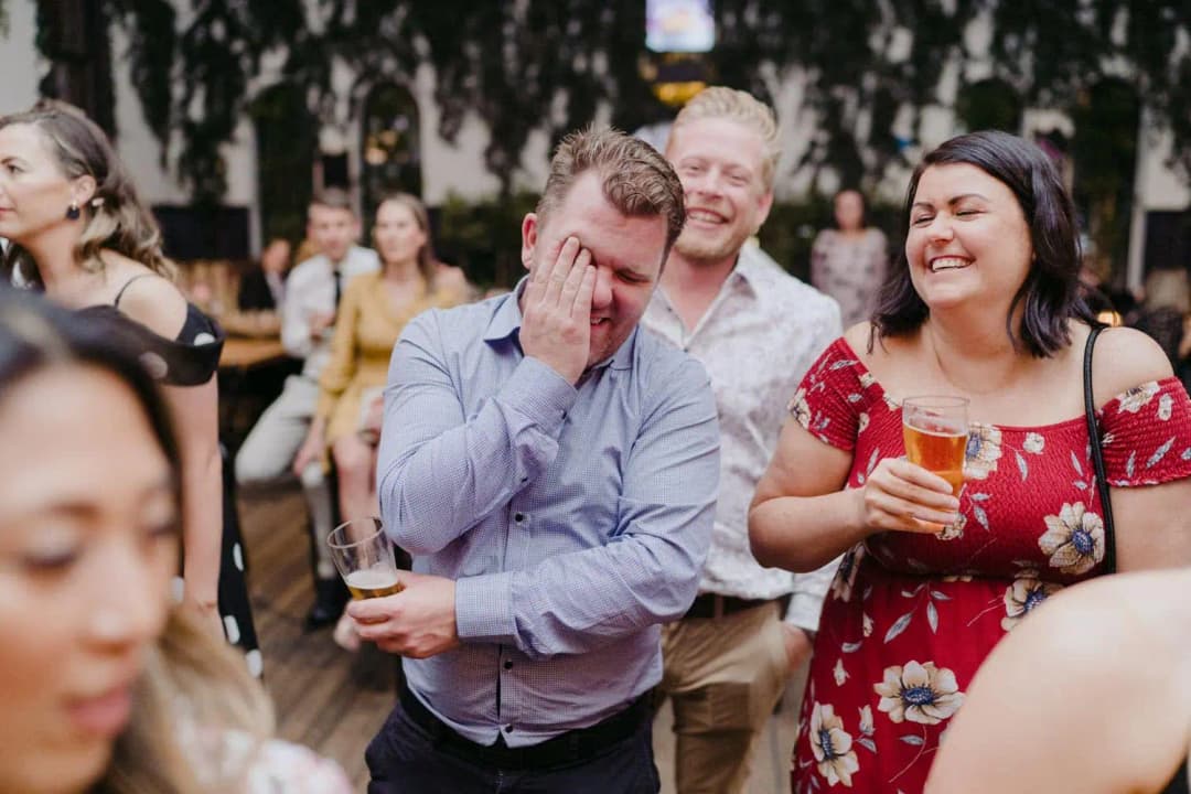 Guest covering his face while laughing with people around him