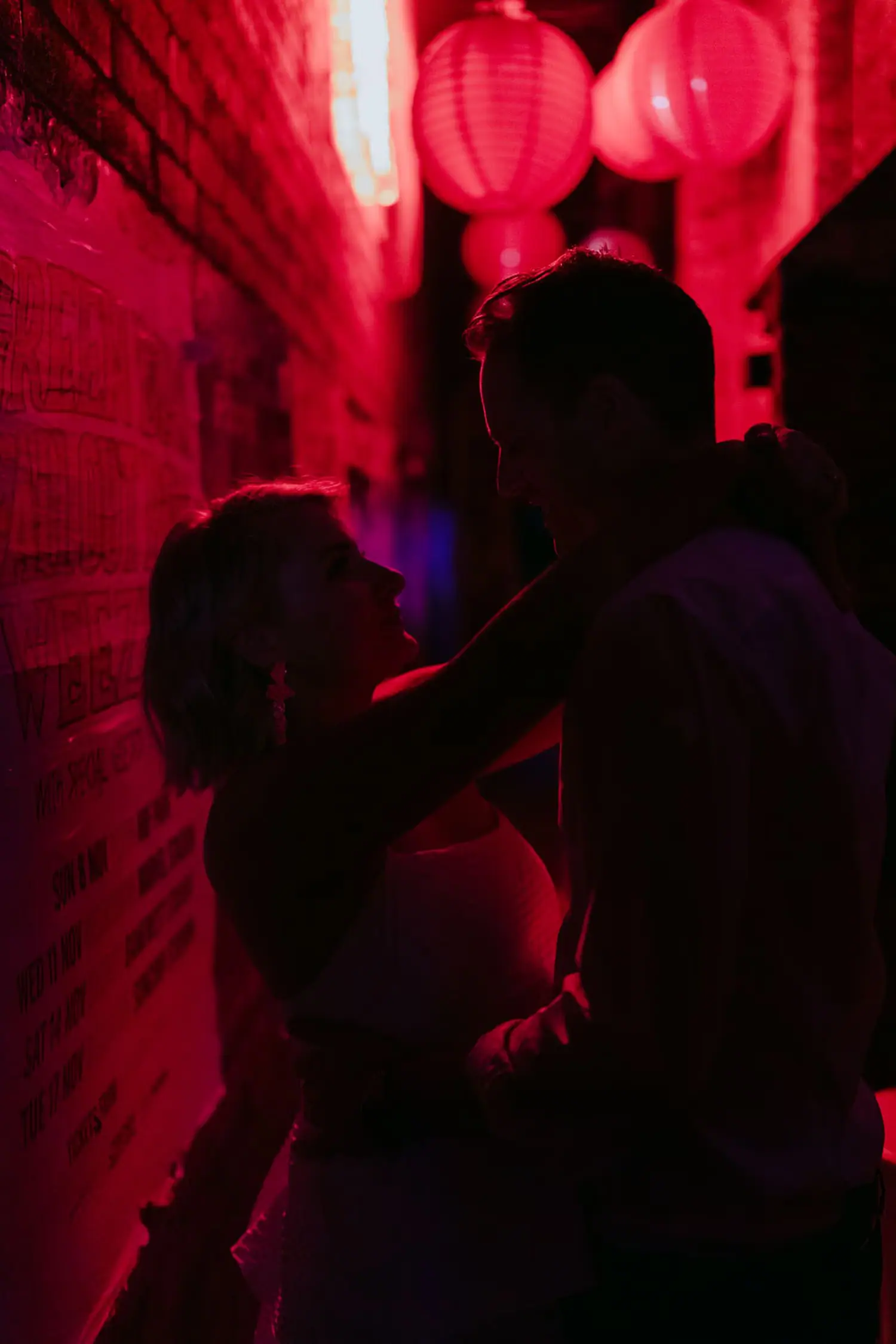 Bride and groom embracing in silhouette beneath glowing red lanterns