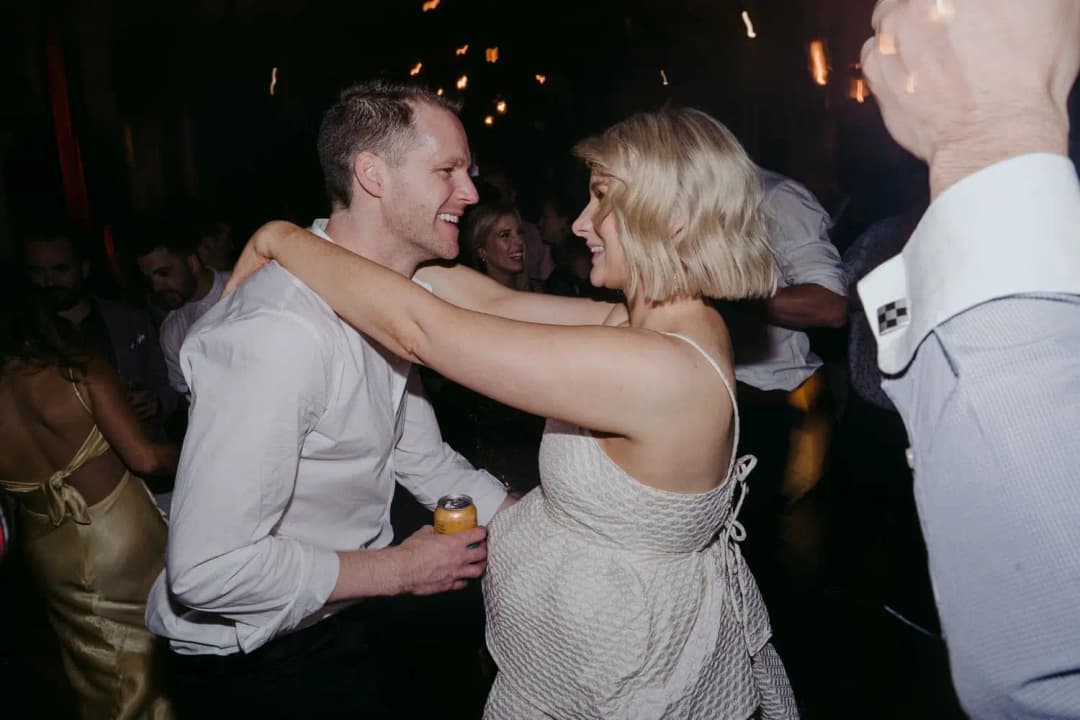Bride with her arms around the groom as they dance together among guests