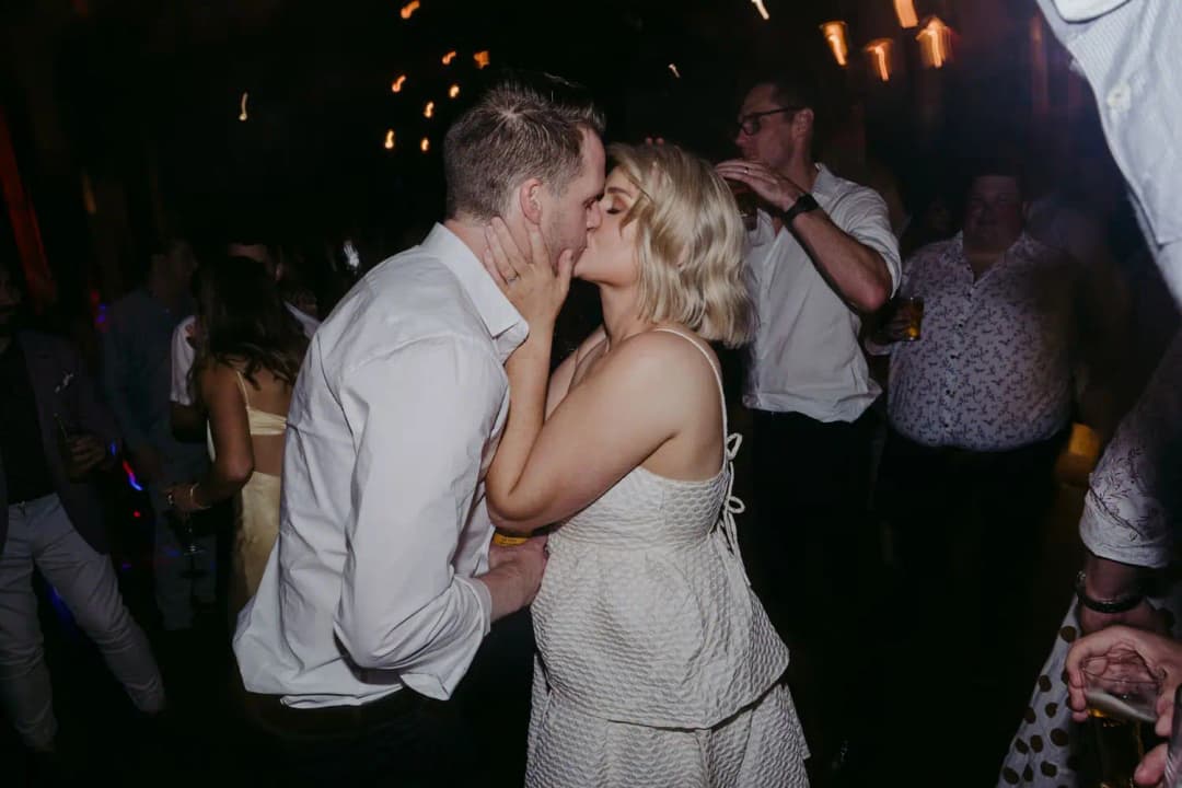 Bride and groom kissing on the dance floor surrounded by guests