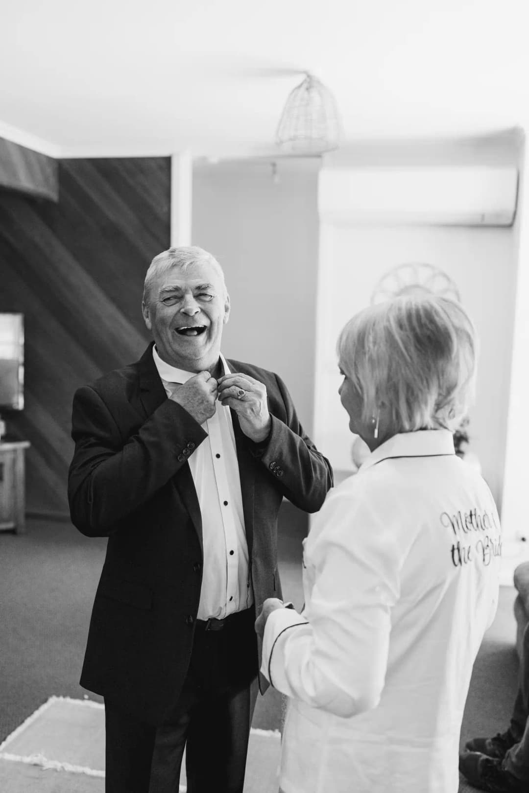 Black-and-white photograph of an older man adjusting his tie with help