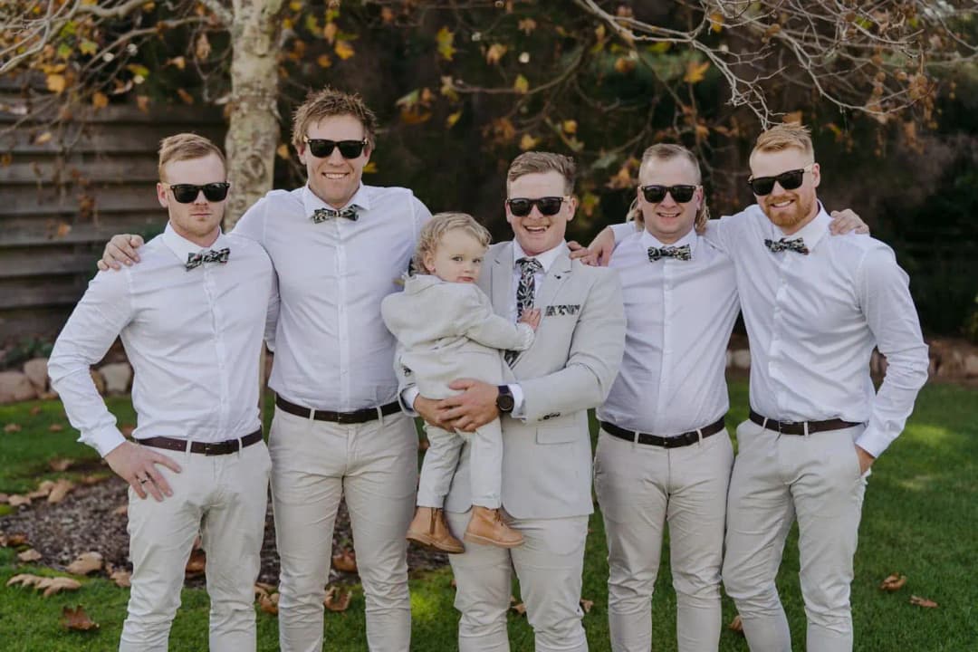 Groom and groomsmen in sunglasses standing outdoors with a small child