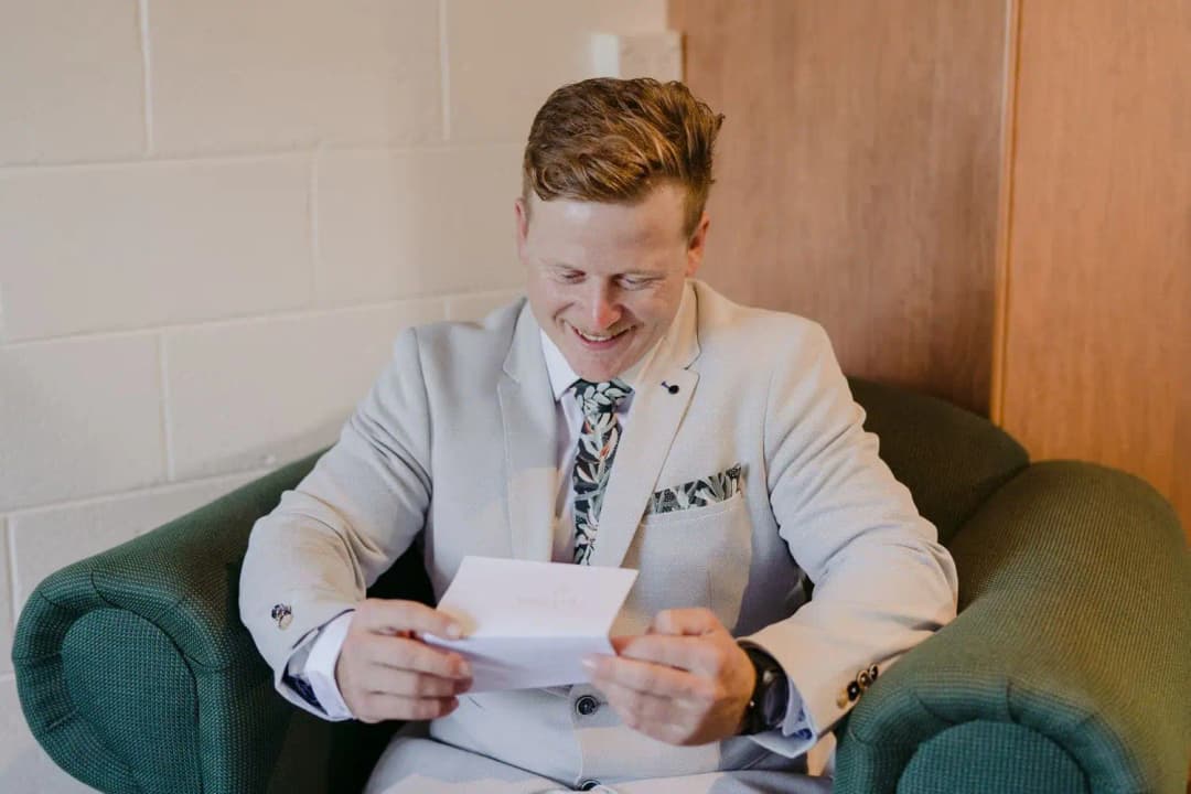 Groom smiling while reading a card in an armchair