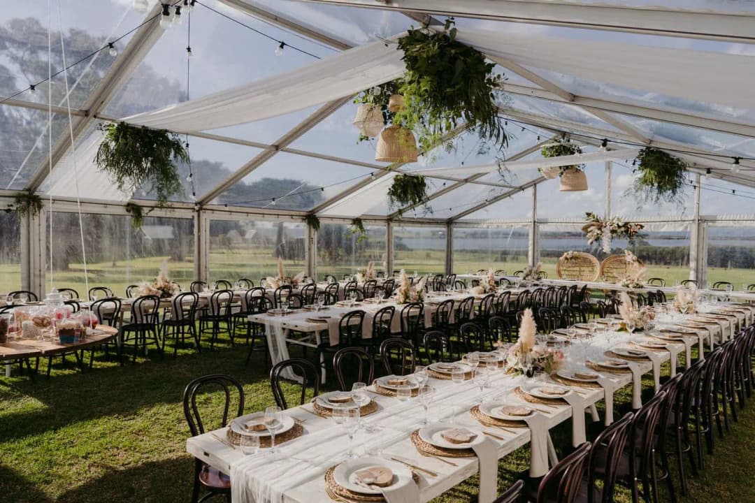 Reception tables and hanging greenery beneath a transparent marquee roof