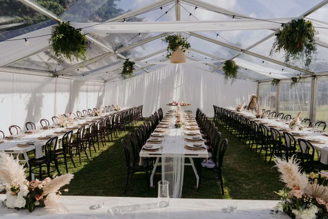 Rows of dining tables inside a clear marquee with hanging plants