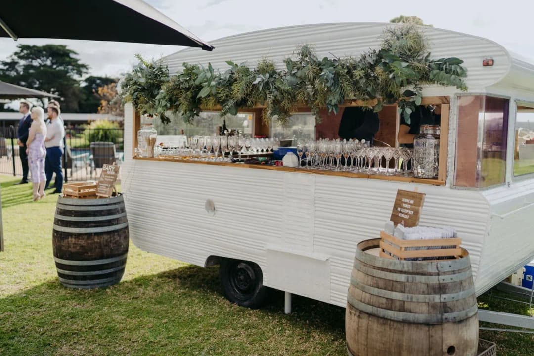 White caravan bar decorated with greenery beside wooden barrels