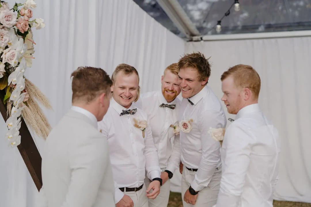 Groom and groomsmen laughing together beside the ceremony flowers