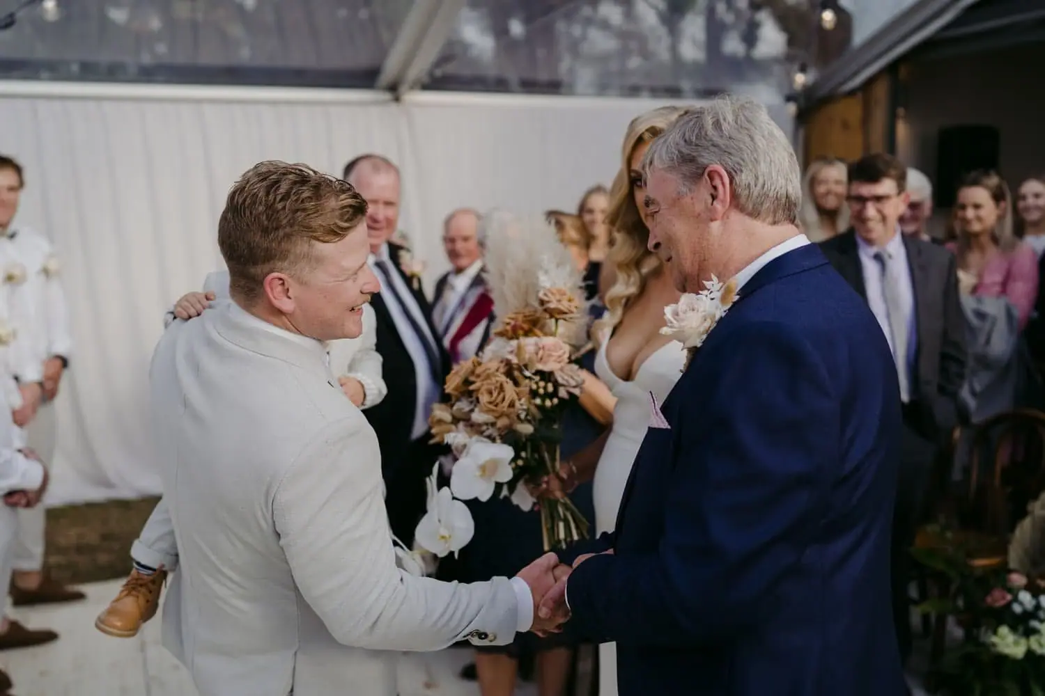 Groom greeting an older man as the bride arrives at the ceremony