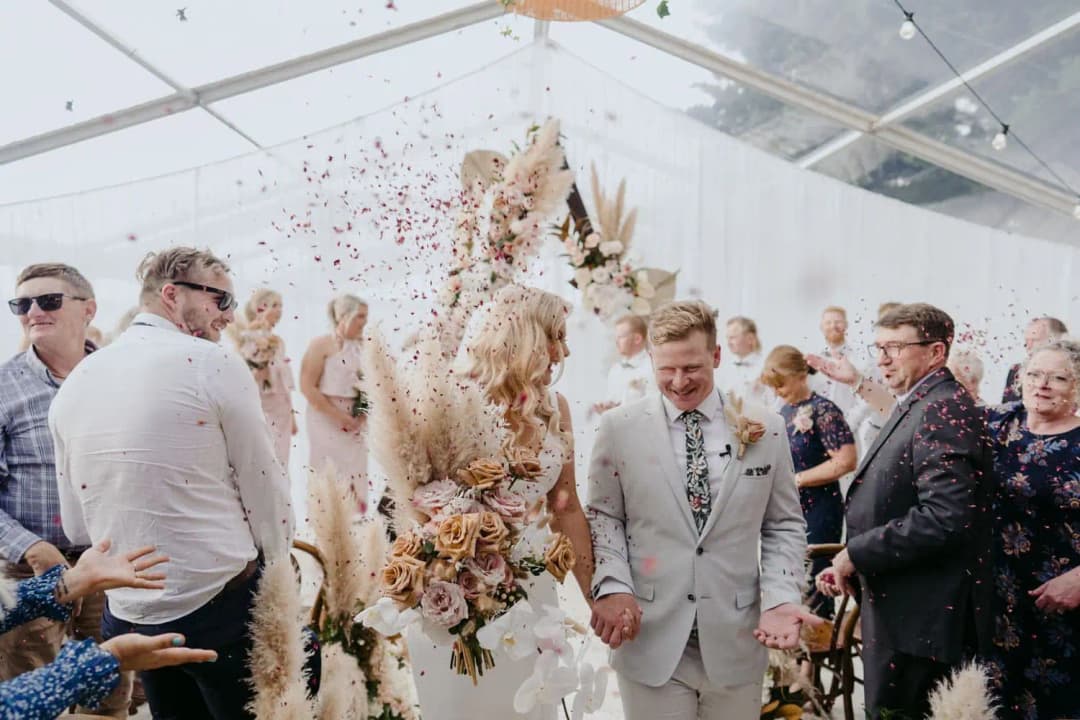 Newlyweds walking through falling petals as their guests applaud