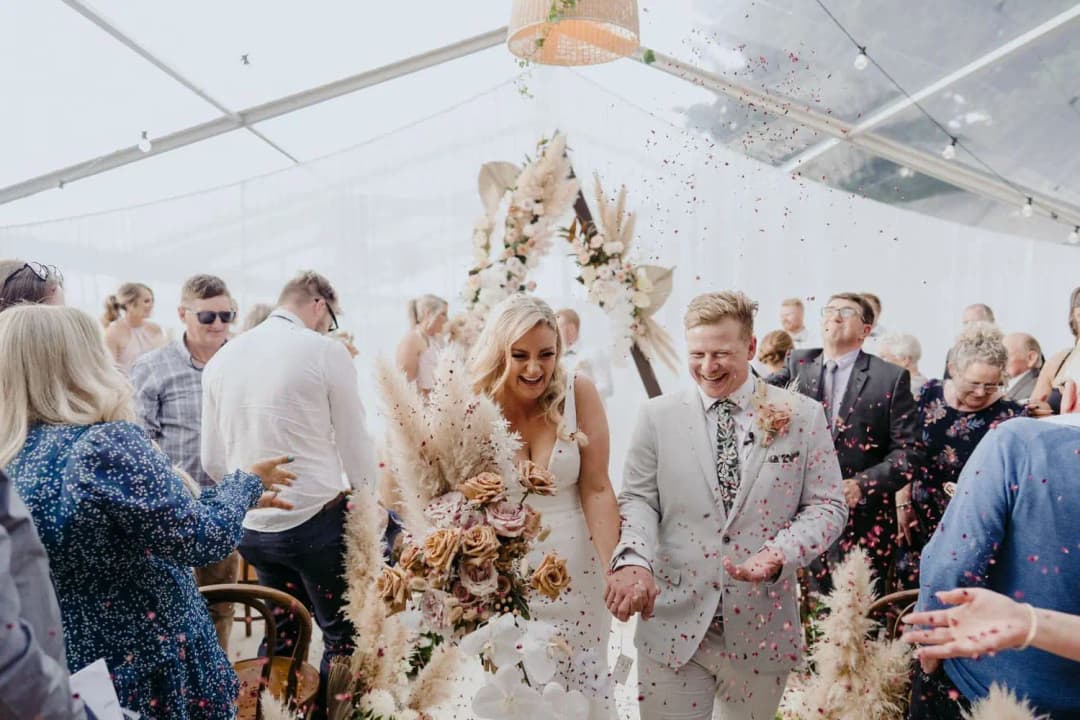 Newlyweds laughing and walking hand in hand between their guests