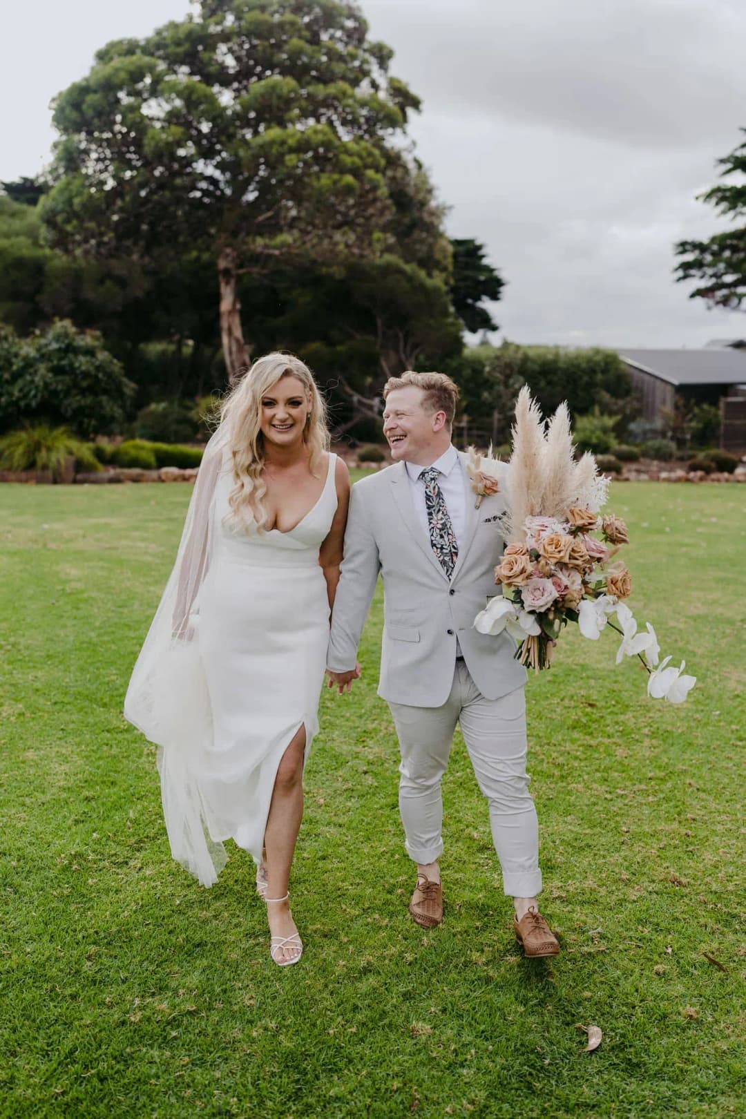 Newlyweds walking hand in hand across a green lawn