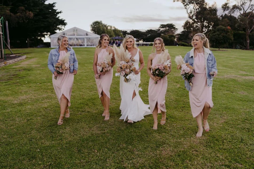 Bride and bridesmaids walking together across a lawn with bouquets